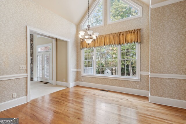 unfurnished dining area featuring a chandelier, hardwood / wood-style floors, french doors, and lofted ceiling