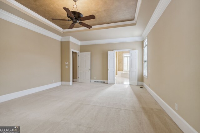 unfurnished bedroom with light carpet, ensuite bathroom, a raised ceiling, and ornamental molding