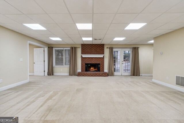 unfurnished living room with french doors, a paneled ceiling, light colored carpet, and a brick fireplace