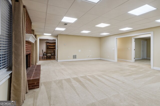 unfurnished living room featuring a paneled ceiling, light carpet, and a brick fireplace