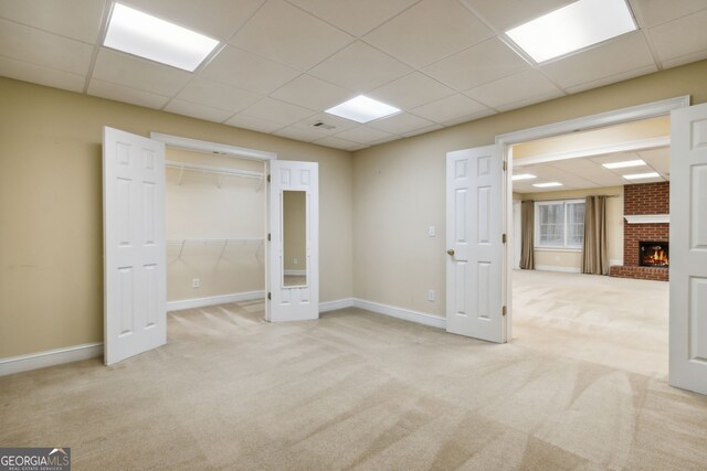 empty room with light carpet, a brick fireplace, and a drop ceiling