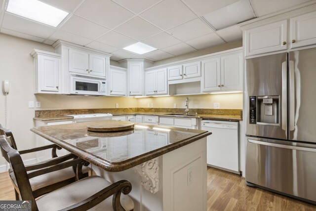 kitchen with white appliances, white cabinets, light wood-type flooring, stone countertops, and a breakfast bar area