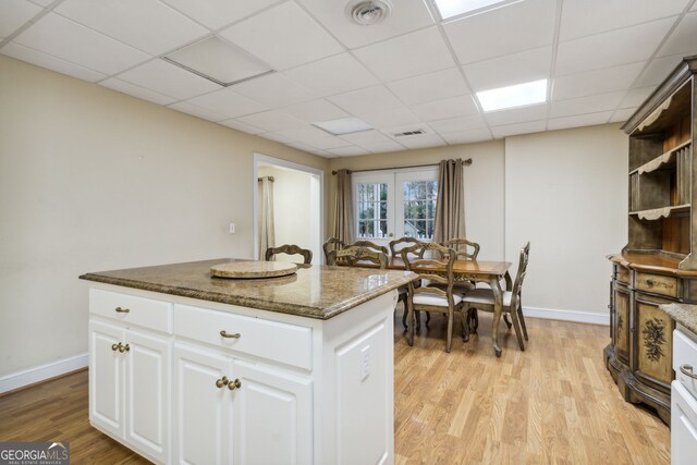 kitchen with a drop ceiling, dark stone counters, white cabinets, light wood-type flooring, and a kitchen island