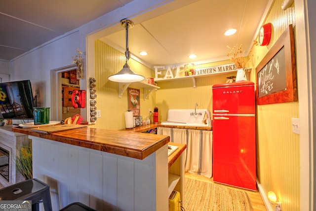 kitchen with kitchen peninsula, refrigerator, light hardwood / wood-style flooring, hanging light fixtures, and butcher block counters