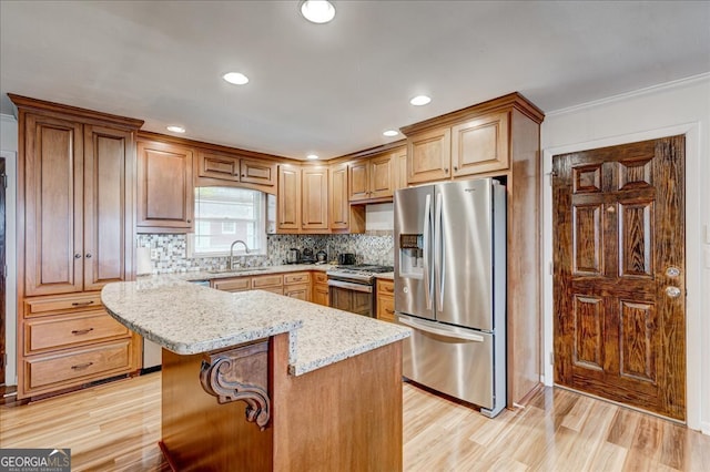 kitchen with sink, stainless steel appliances, light stone counters, light hardwood / wood-style flooring, and a kitchen island