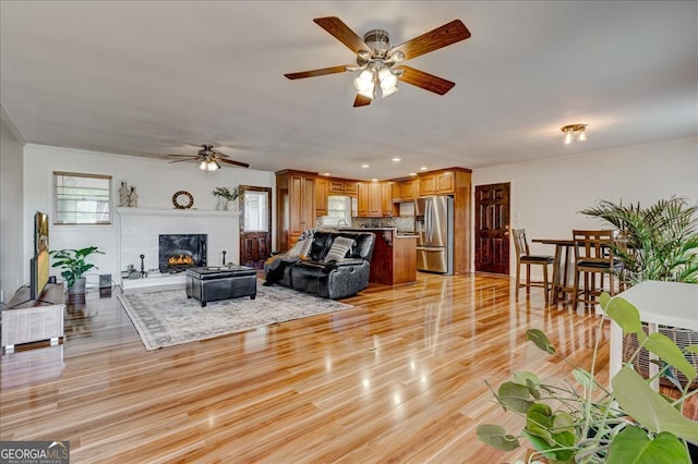 living room featuring ceiling fan, crown molding, light wood-type flooring, and a fireplace