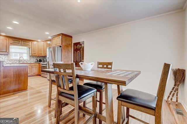 dining room with light wood-type flooring, crown molding, and sink