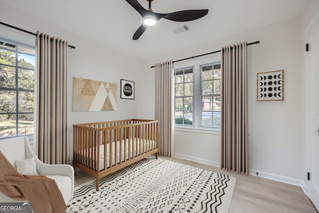 bedroom featuring multiple windows, ceiling fan, light hardwood / wood-style flooring, and a nursery area