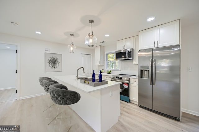 kitchen featuring pendant lighting, white cabinets, light hardwood / wood-style flooring, appliances with stainless steel finishes, and a kitchen bar