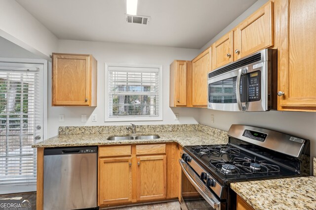 kitchen with appliances with stainless steel finishes, light stone counters, light brown cabinetry, and sink