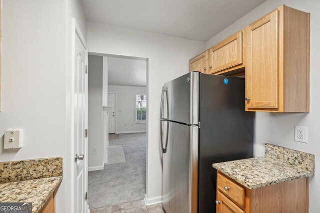 kitchen with light brown cabinets, light colored carpet, light stone countertops, and stainless steel refrigerator