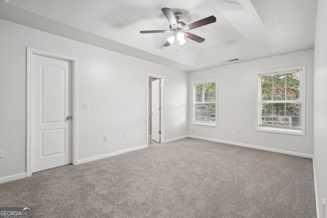 carpeted spare room featuring ceiling fan and a raised ceiling