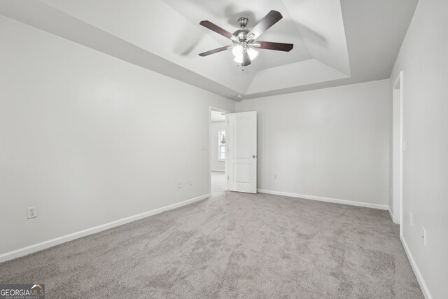 carpeted spare room featuring a tray ceiling and ceiling fan