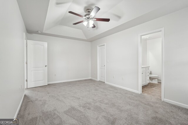 unfurnished bedroom featuring a raised ceiling, ensuite bath, ceiling fan, and light carpet