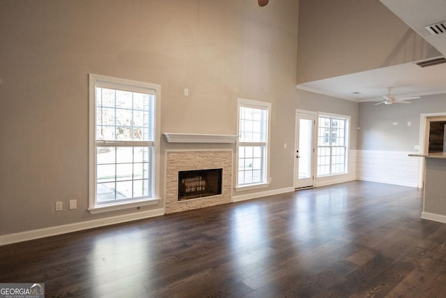 unfurnished living room featuring dark hardwood / wood-style floors, ceiling fan, a stone fireplace, and a towering ceiling