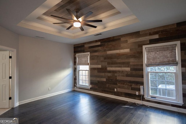 empty room with a raised ceiling, plenty of natural light, dark wood-type flooring, and wood walls