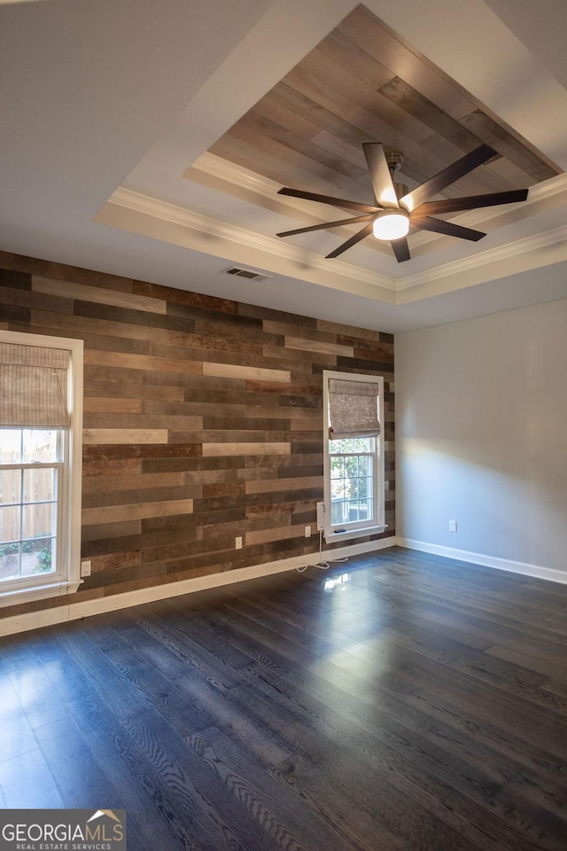 unfurnished room featuring ceiling fan, dark wood-type flooring, a raised ceiling, crown molding, and wooden walls