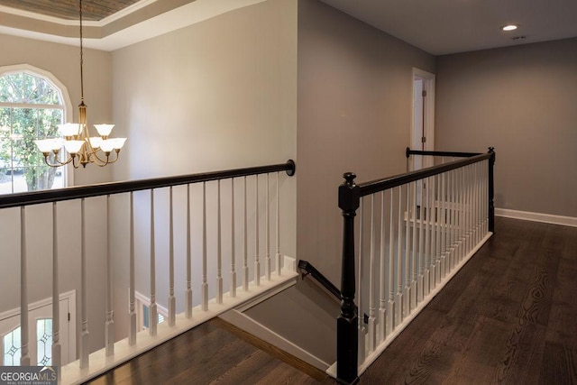 staircase with a raised ceiling, hardwood / wood-style flooring, ornamental molding, and a notable chandelier