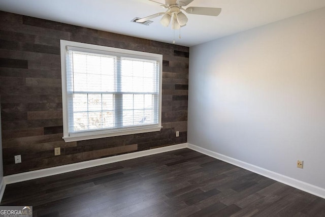 spare room featuring ceiling fan, dark wood-type flooring, and wood walls