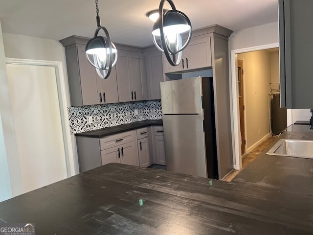 kitchen with gray cabinets, hanging light fixtures, stainless steel refrigerator, and tasteful backsplash