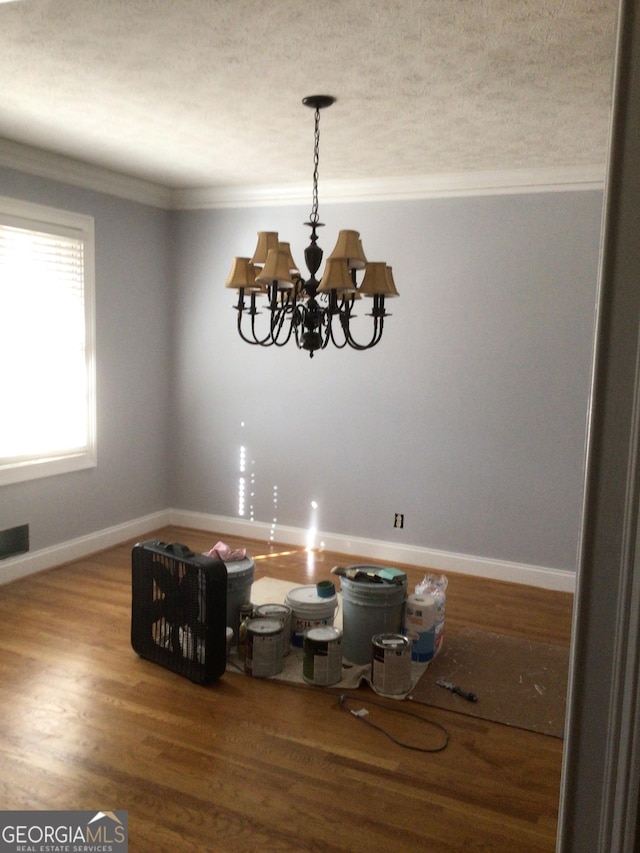 unfurnished dining area featuring hardwood / wood-style floors, ornamental molding, and a notable chandelier