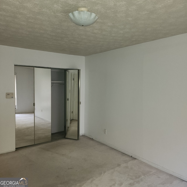 unfurnished bedroom featuring a textured ceiling, light carpet, and a closet