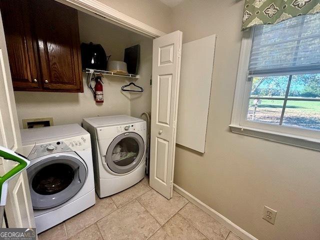 clothes washing area featuring washer and dryer, cabinet space, baseboards, and light tile patterned floors