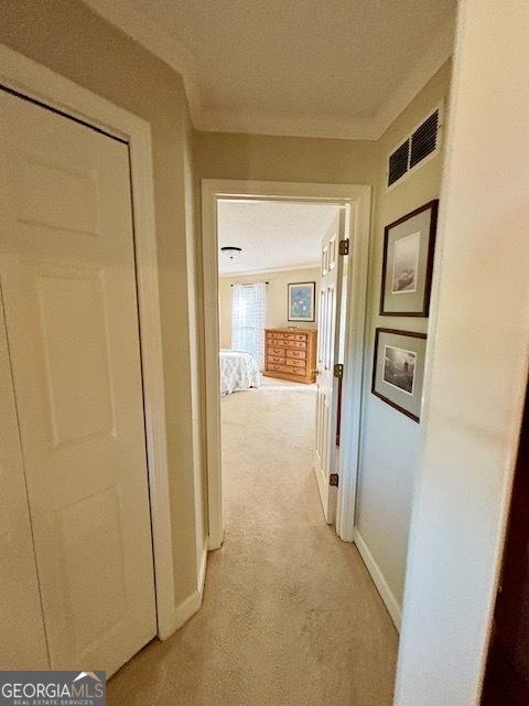 hall with baseboards, light colored carpet, visible vents, and crown molding