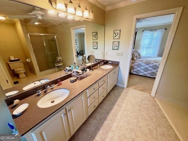 ensuite bathroom featuring crown molding, a stall shower, and a sink