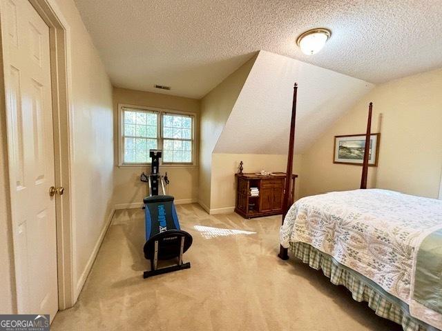 bedroom featuring light colored carpet, vaulted ceiling, a textured ceiling, and baseboards