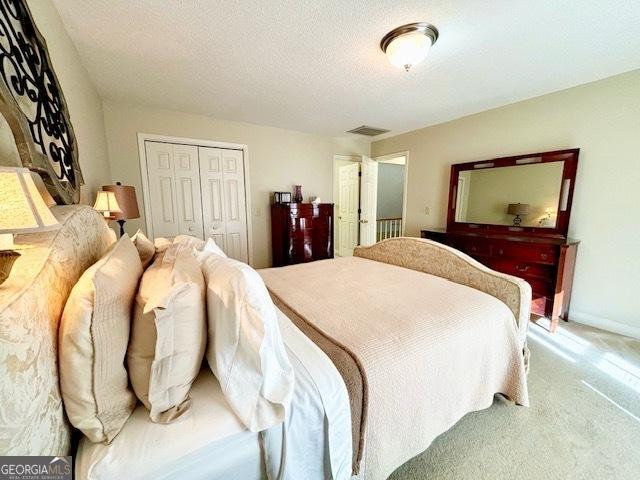 bedroom with a closet, visible vents, light carpet, a textured ceiling, and baseboards