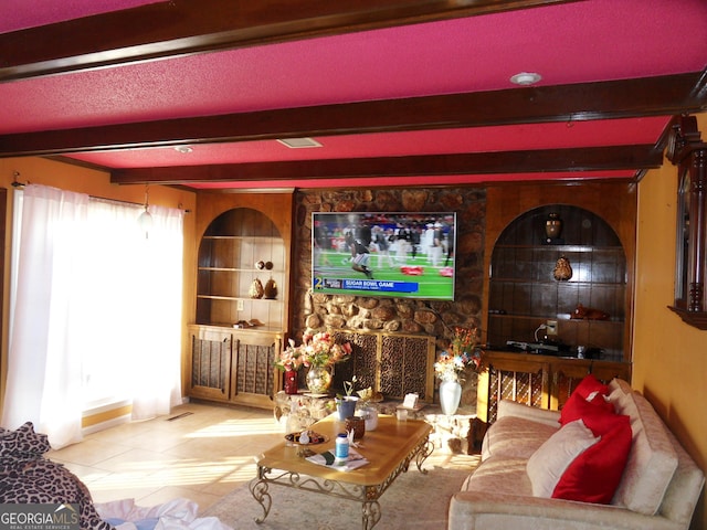 living room with beam ceiling, a stone fireplace, built in features, and light tile patterned floors