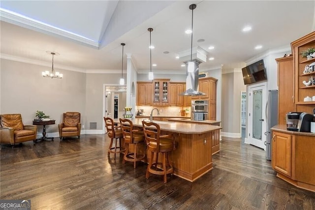 kitchen featuring decorative light fixtures, a notable chandelier, a breakfast bar, stainless steel appliances, and wall chimney exhaust hood