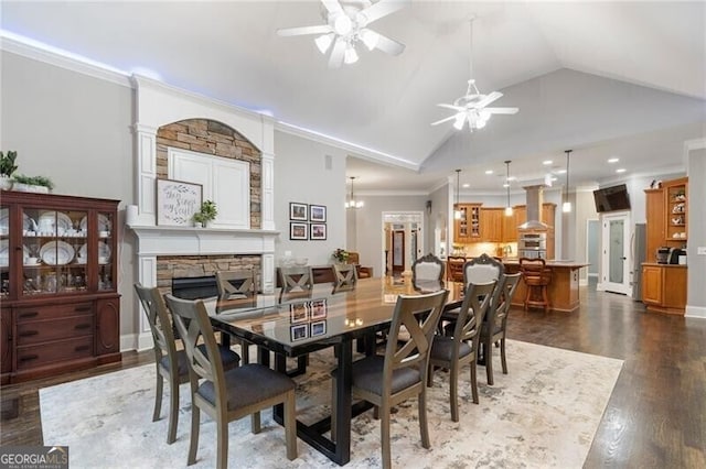 dining room with dark hardwood / wood-style floors, lofted ceiling, ornamental molding, ceiling fan, and a stone fireplace