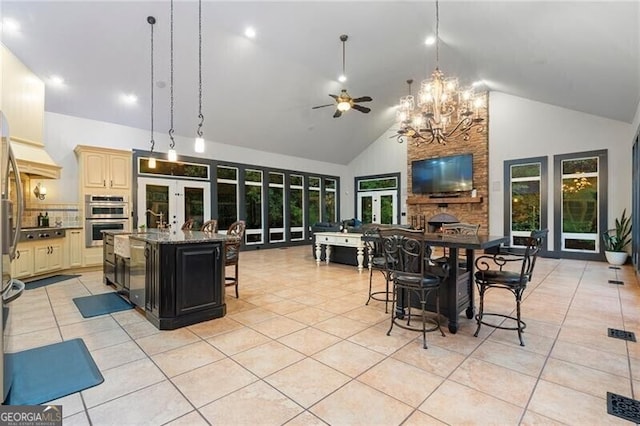 kitchen featuring dark stone counters, ceiling fan, high vaulted ceiling, light tile patterned floors, and a center island with sink