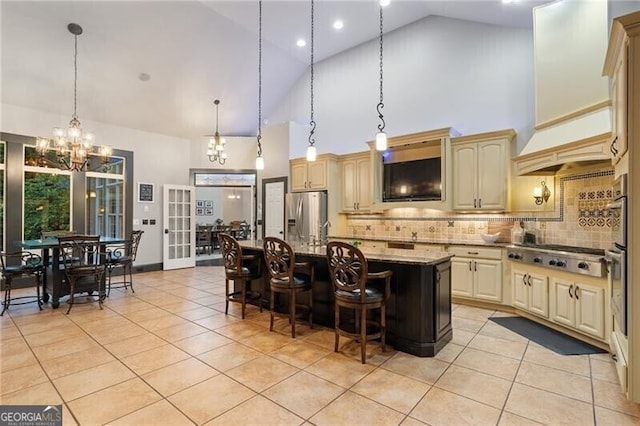 kitchen featuring decorative light fixtures, dark stone countertops, decorative backsplash, a kitchen island with sink, and appliances with stainless steel finishes