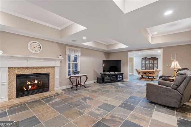 living room featuring a raised ceiling, a tiled fireplace, and crown molding