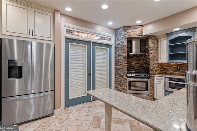 kitchen featuring light stone countertops, backsplash, appliances with stainless steel finishes, and wall chimney exhaust hood