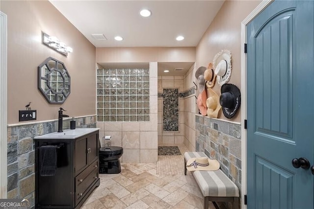 bathroom featuring toilet, vanity, tile walls, and tiled shower