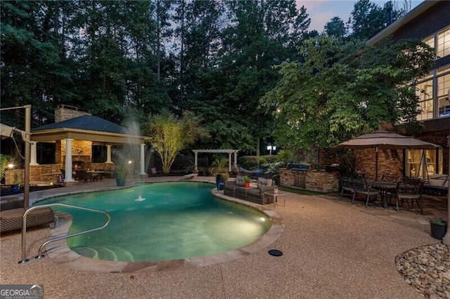 pool at dusk with exterior kitchen and a patio