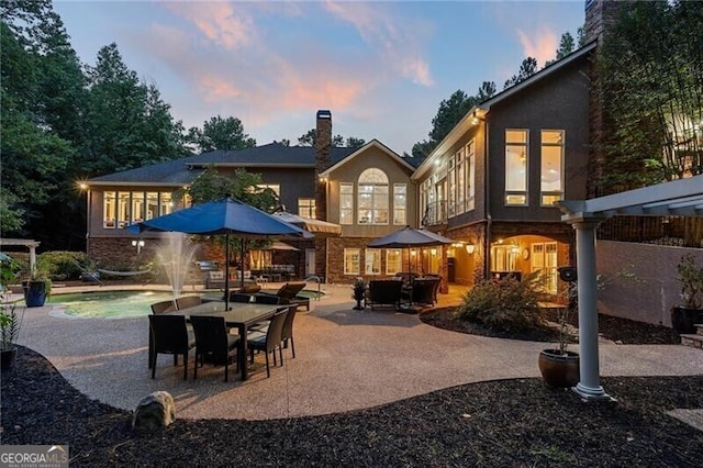 back house at dusk with a swimming pool, pool water feature, and a patio