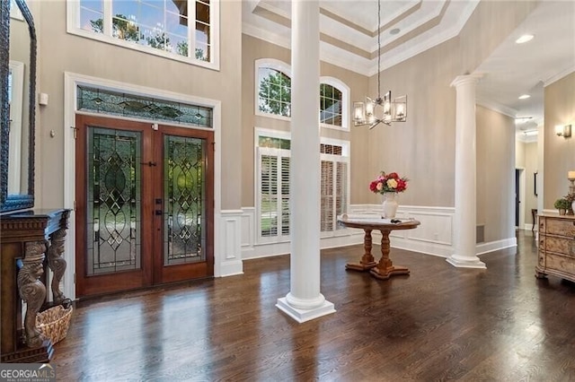 entrance foyer featuring a towering ceiling, an inviting chandelier, ornamental molding, and ornate columns