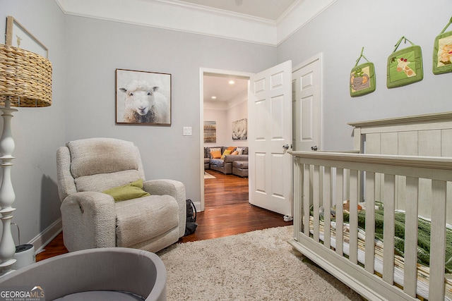 bedroom with crown molding, dark wood-type flooring, and a nursery area