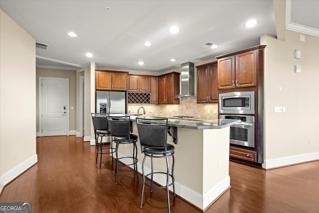 kitchen featuring a kitchen breakfast bar, wall chimney exhaust hood, dark hardwood / wood-style floors, an island with sink, and stainless steel appliances