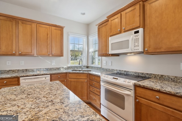 kitchen featuring light stone counters, white appliances, and sink