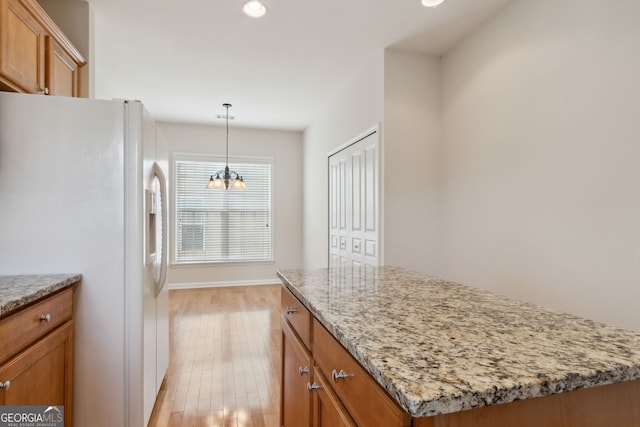 kitchen with light stone countertops, light wood-type flooring, pendant lighting, white fridge, and a kitchen island