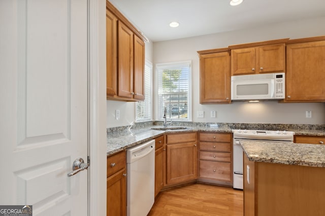 kitchen with light stone countertops, light wood-type flooring, white appliances, and sink