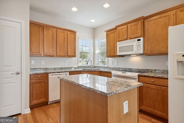 kitchen featuring white appliances, sink, light wood-type flooring, a kitchen island, and light stone counters