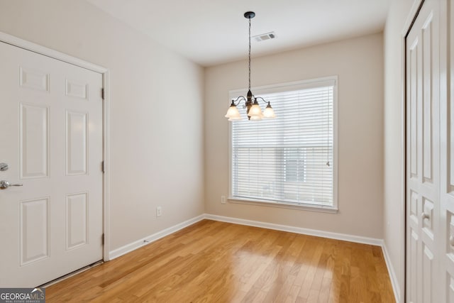 unfurnished dining area with wood-type flooring and a notable chandelier