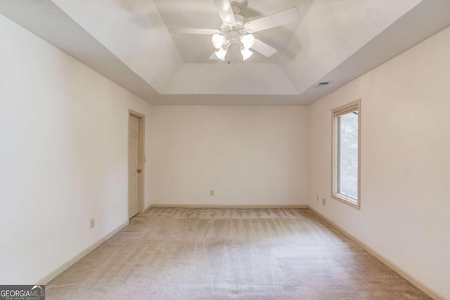 unfurnished room with a raised ceiling, ceiling fan, and carpet flooring